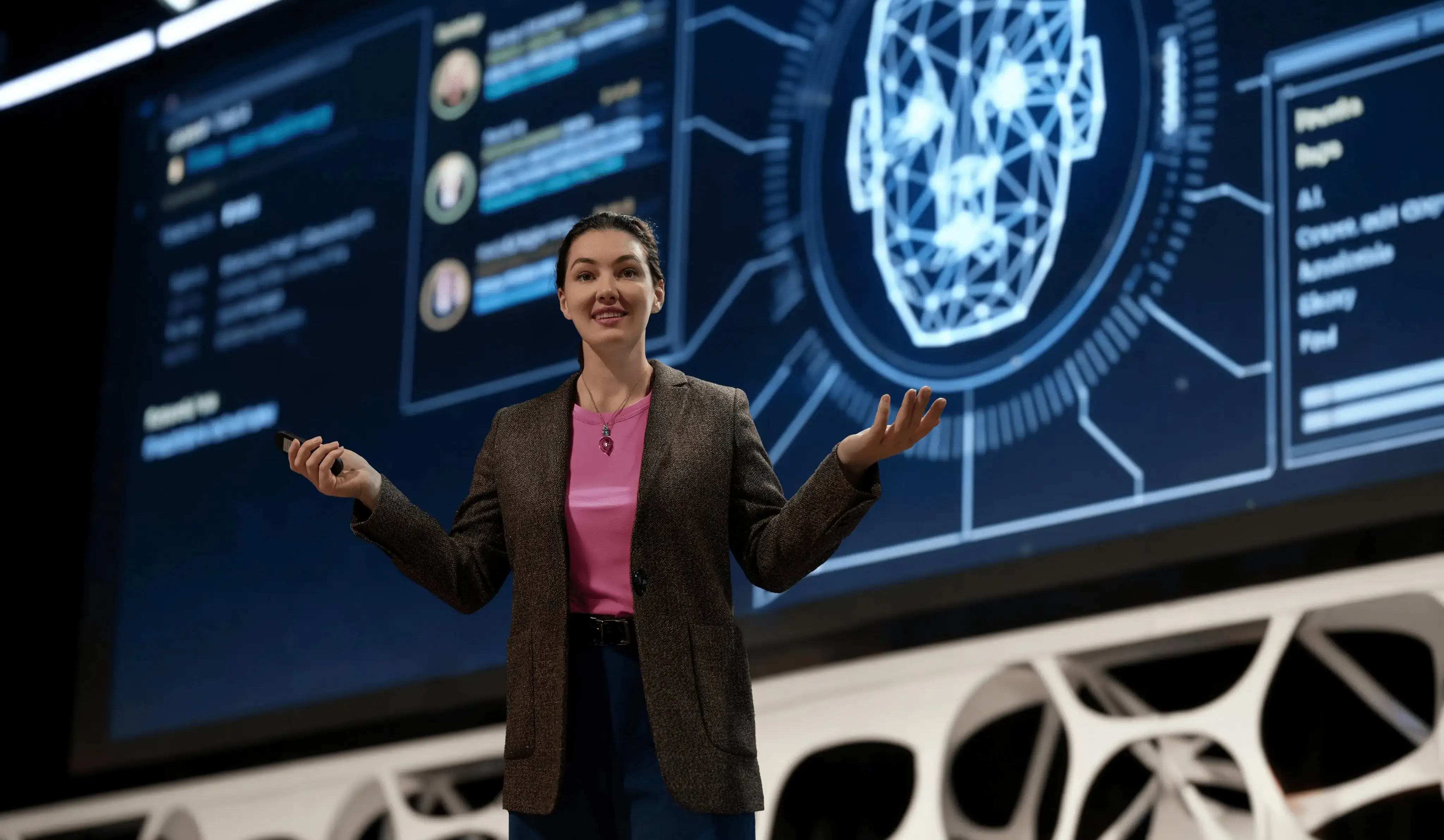 A speaker stands on stage presenting in front of a large screen featuring a digital brain graphic and AI-themed data.